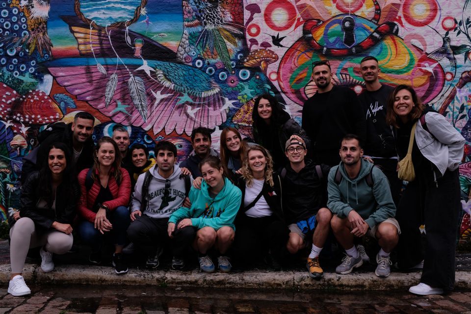 Un viaje en grupo de WeRoad posando para una foto grupal frente a un colorido e intrincado mural de grafiti en una calle de la ciudad.