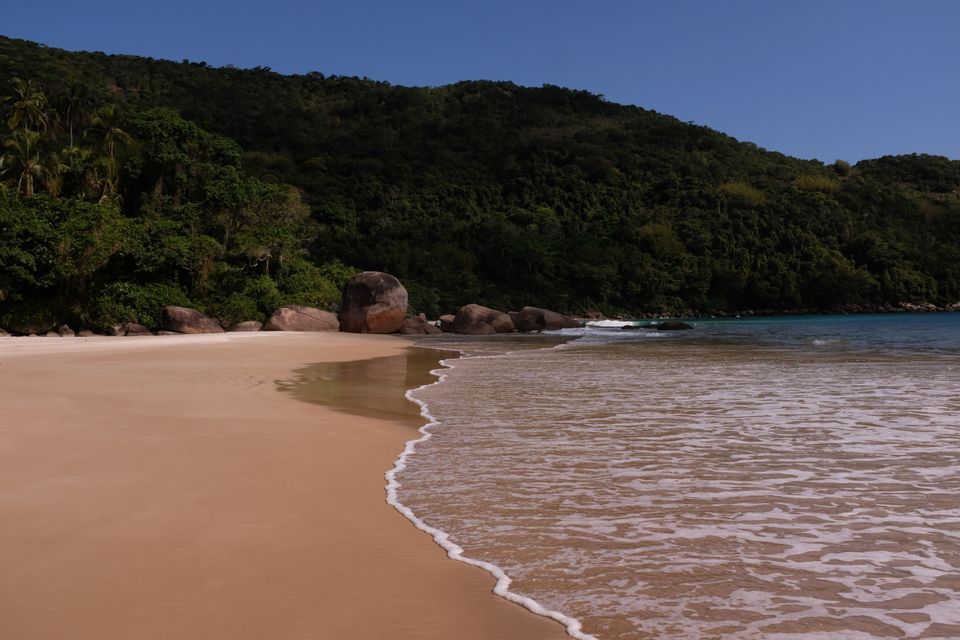 La costa de una playa de arena apartada donde las suaves olas besan la arena, con una exuberante colina verde de fondo.
