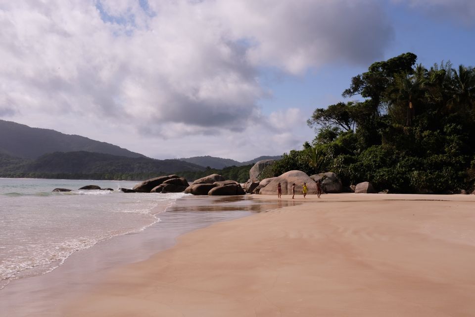 Eine WeRoad Gruppenreise entlang eines breiten Sandstrandes neben großen Felsen und einem üppigen, bewaldeten Hügel.