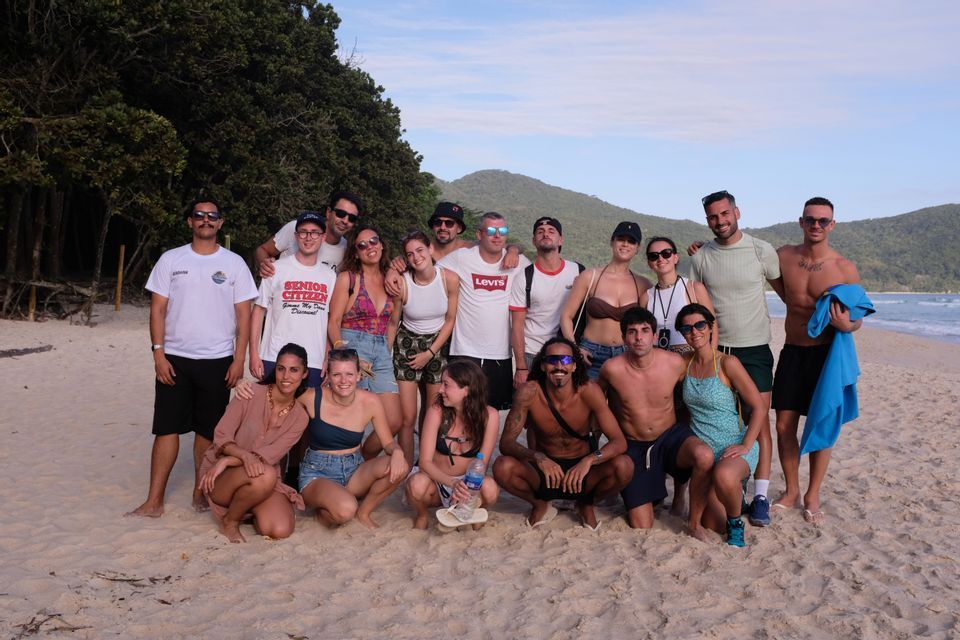 Eine WeRoad-Gruppenreise posiert für ein Foto an einem Sandstrand, mit Wald und Hügeln im Hintergrund.