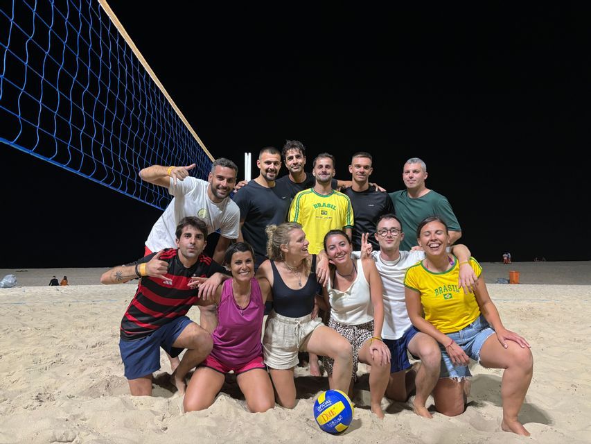 Eine WeRoad-Gruppe macht ein Gruppenfoto am Sandstrand bei Nacht vor einem Volleyballnetz.