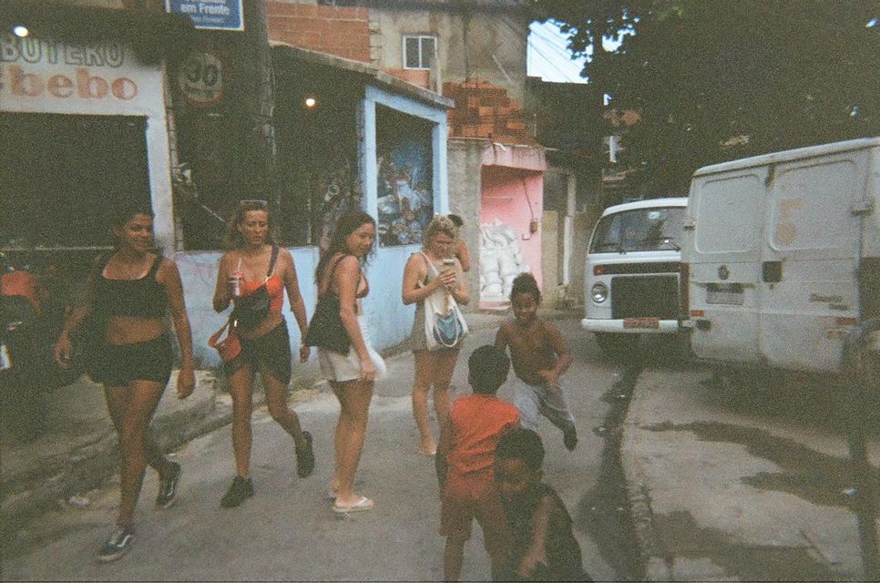 Un gruppo di donne in viaggio con WeRoad cammina per strada mentre bambini del posto giocano nelle vicinanze, con edifici e un furgone sullo sfondo.