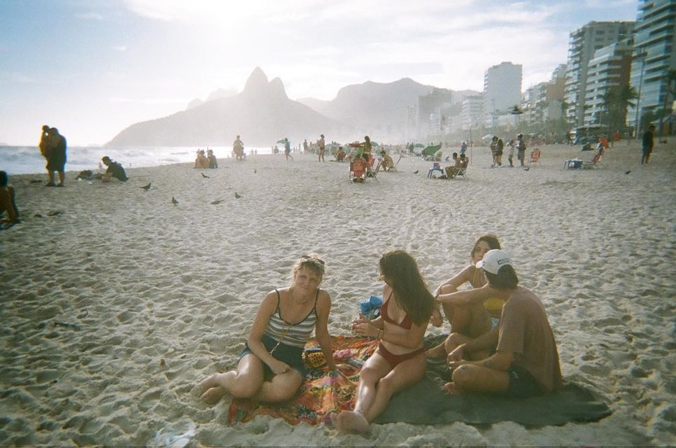 Eine WeRoad-Gruppenreise mit vier Personen, die auf Handtüchern an einem belebten Strand sitzen, mit Bergen und einer Stadt im Hintergrund.