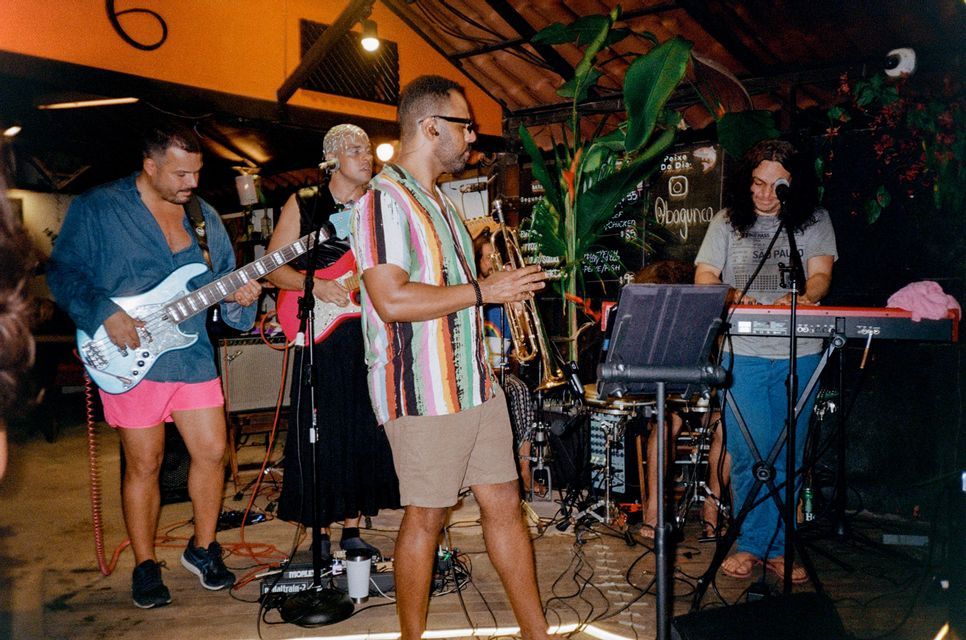Eine vierköpfige Band, bestehend aus Bassist, Gitarrist, Trompeter und Keyboarder, spielt auf einer schwach beleuchteten Bühne.
