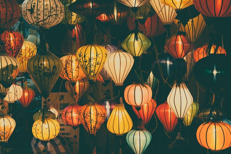Decine di colorate lanterne di carta asiatiche illuminate, con disegni dipinti, sono appese fitte nell'oscurità.