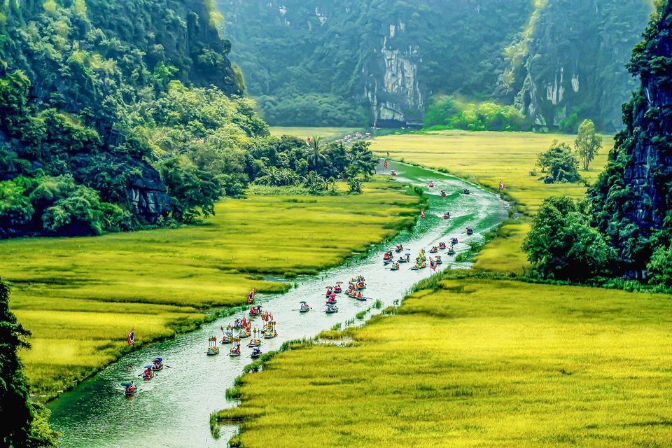 Un viaggio di gruppo WeRoad in piccole imbarcazioni che scende lungo un fiume tortuoso, circondato da risaie verde brillante e montagne rigogliose.
