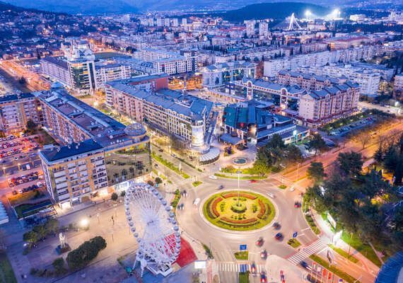 Veduta aerea di un paesaggio urbano al tramonto, con una ruota panoramica illuminata e una rotonda trafficata.