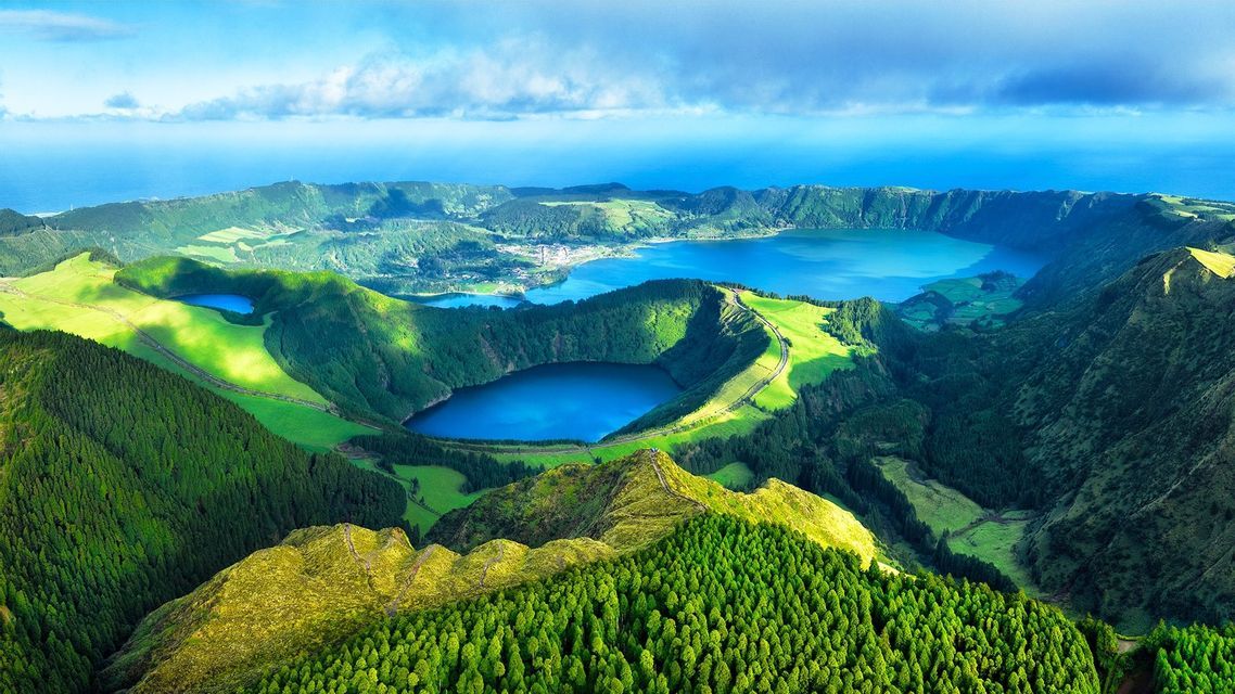 Vue aérienne de plusieurs lacs de cratère bleus nichés dans des collines volcaniques verdoyantes, avec l'océan en arrière-plan.