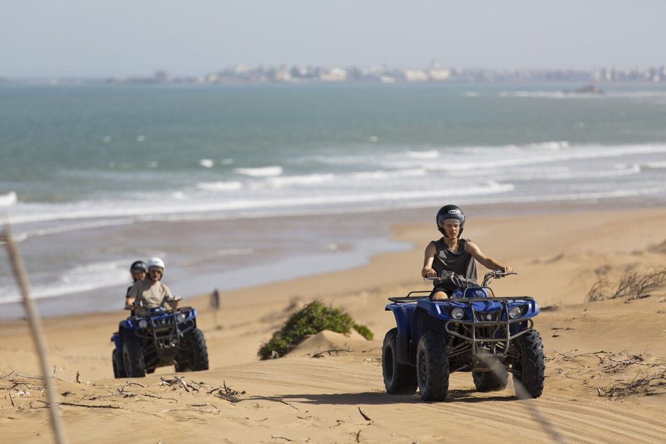 A WeRoad group trip riding quad bikes on sand dunes along a beach with the ocean in the background.