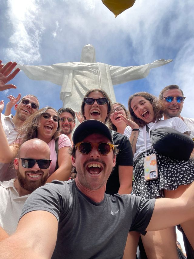 Un viaggio di gruppo WeRoad scatta un selfie sorridente con la statua del Cristo Redentore sullo sfondo.