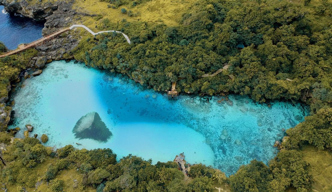 Vista aerea di una laguna naturale con acqua turchese cristallina, circondata da fitta foresta verde e scogliere rocciose.