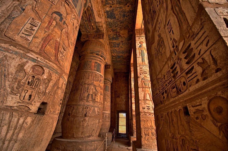 Imponentes pilares de piedra con coloridas tallas jeroglíficas llenan el interior de un templo antiguo.