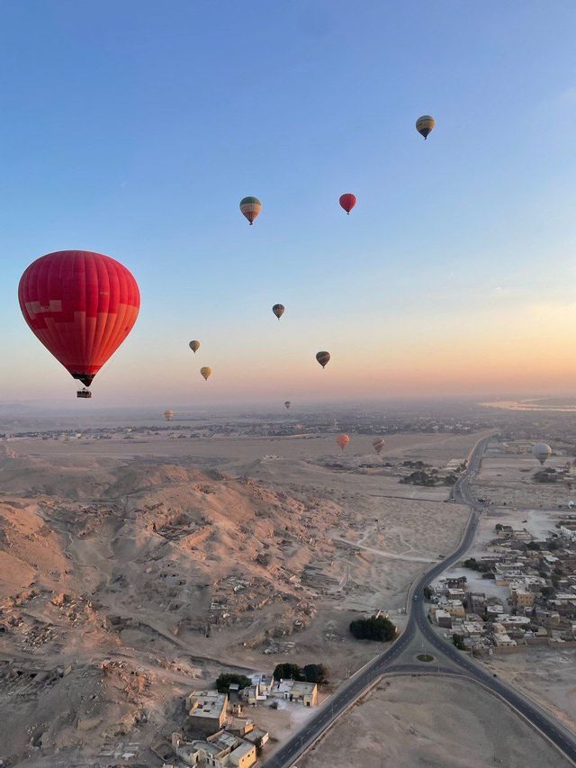 Una vista aérea de múltiples globos aerostáticos flotando sobre un paisaje desértico y un pueblo al amanecer.