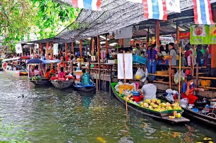 Un bullicioso mercado flotante en un canal, con vendedores en botes ofreciendo fruta y gente comprando desde un muelle cubierto.