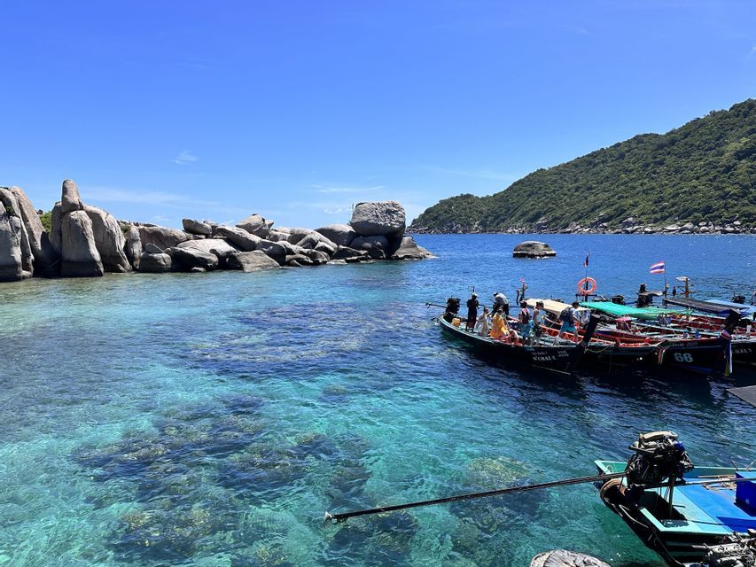 Un viaggio di gruppo WeRoad su barche long-tail in una baia con acqua turchese cristallina e costa rocciosa.