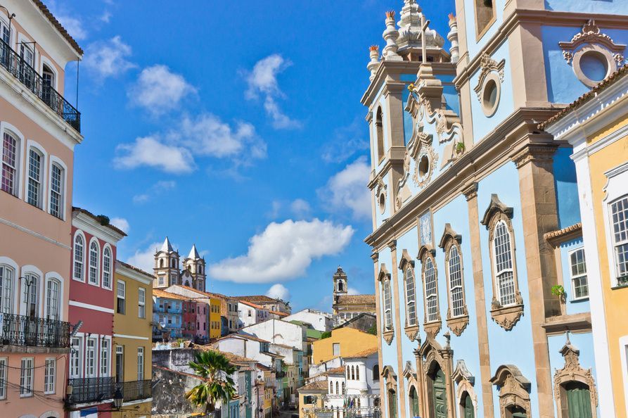 Colorful colonial buildings and a light blue church line a street under a bright blue sky with white clouds.