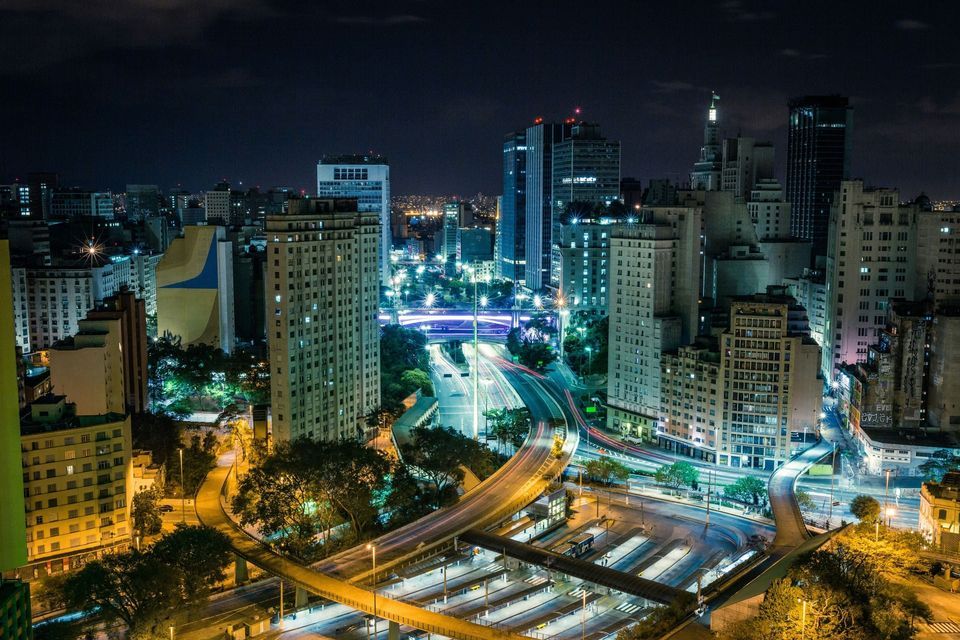Silueta urbana nocturna con edificios iluminados y estelas de luz de tráfico en una autopista sinuosa.