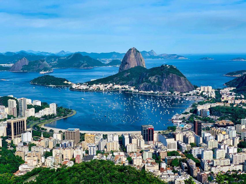 Vista aérea de una ciudad costera, una bahía llena de veleros y un prominente pico montañoso bajo un cielo azul claro