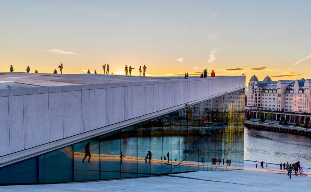 Silhouetten von Menschen stehen auf dem schrägen Dach eines modernen Gebäudes mit großen Glasfenstern während eines goldenen Sonnenuntergangs.