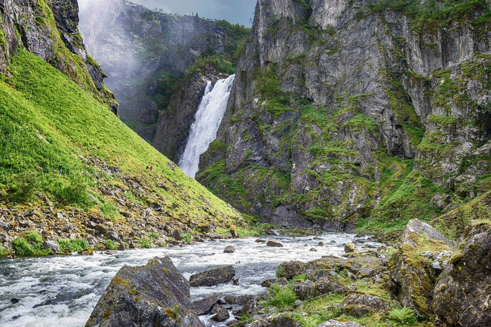 Eine WeRoad-Gruppenreise beim Wandern an einem steilen grünen Hang, neben einem mächtigen Wasserfall, der in einen felsigen Fluss mündet.