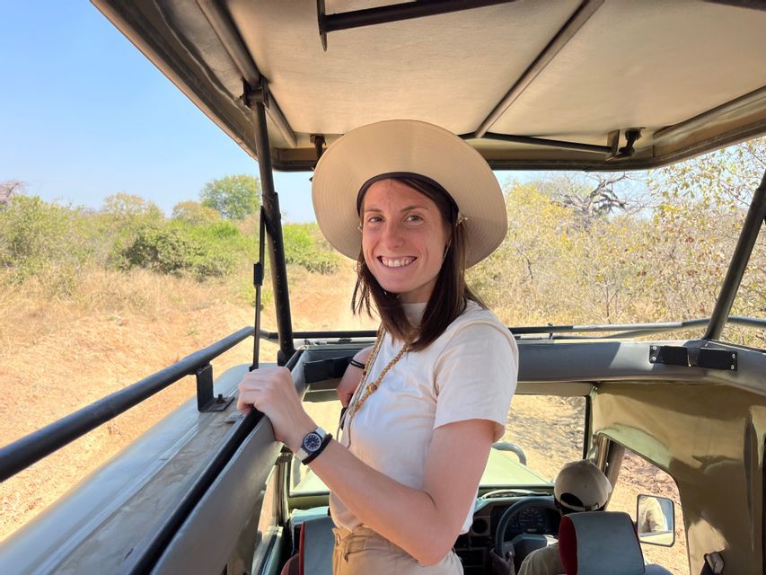 Una donna sorridente con un cappello in piedi su una jeep aperta durante un safari di gruppo WeRoad in un paesaggio soleggiato.