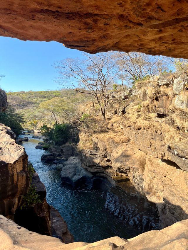Vista da uno strapiombo roccioso su un fiume che serpeggia in un canyon soleggiato, con alberi e cielo limpido.