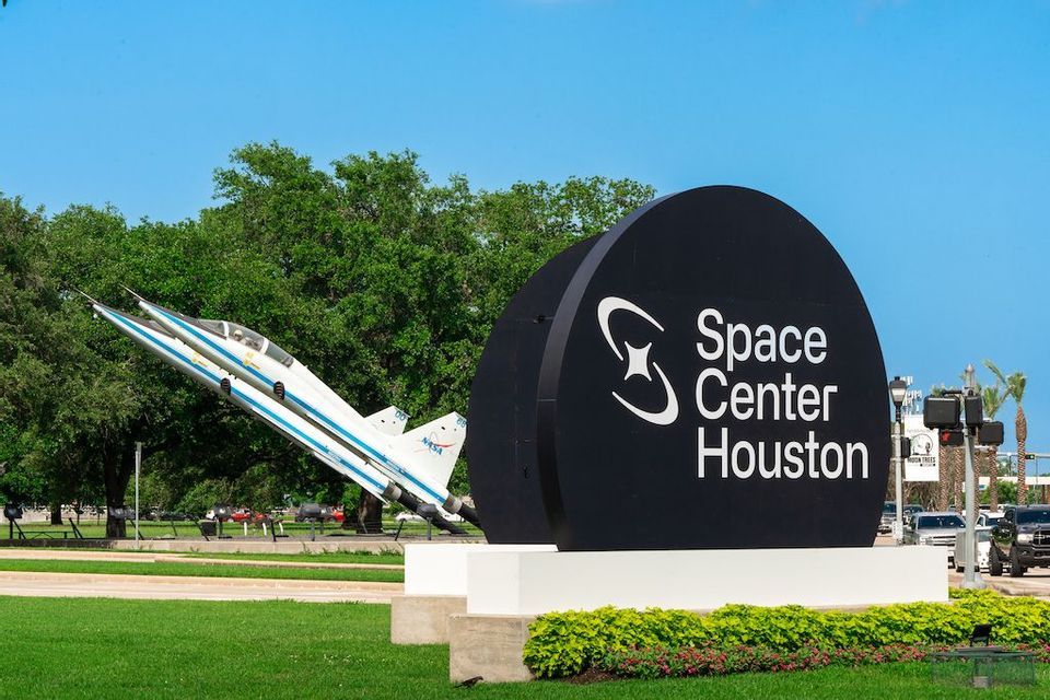 Il grande cartello nero dello Space Center Houston accanto a un modello di jet NASA bianco su un prato verde.