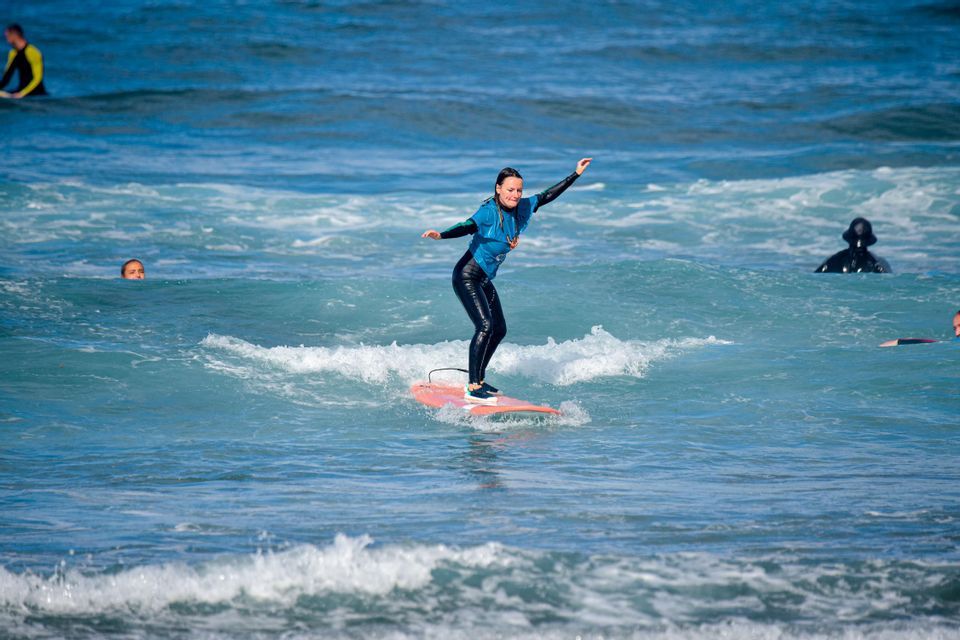 Una donna di un gruppo WeRoad in muta riesce a stare in piedi sulla sua tavola da surf su un'onda blu.