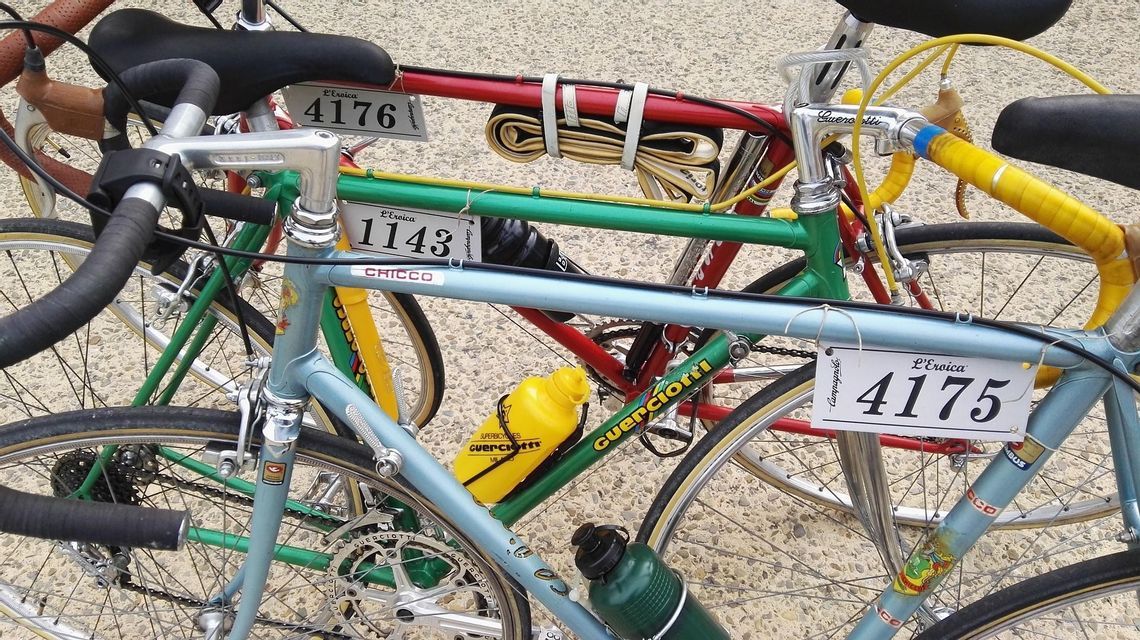Primo piano di diverse biciclette da corsa vintage colorate con i numeri di gara de L'Eroica attaccati ai telai.