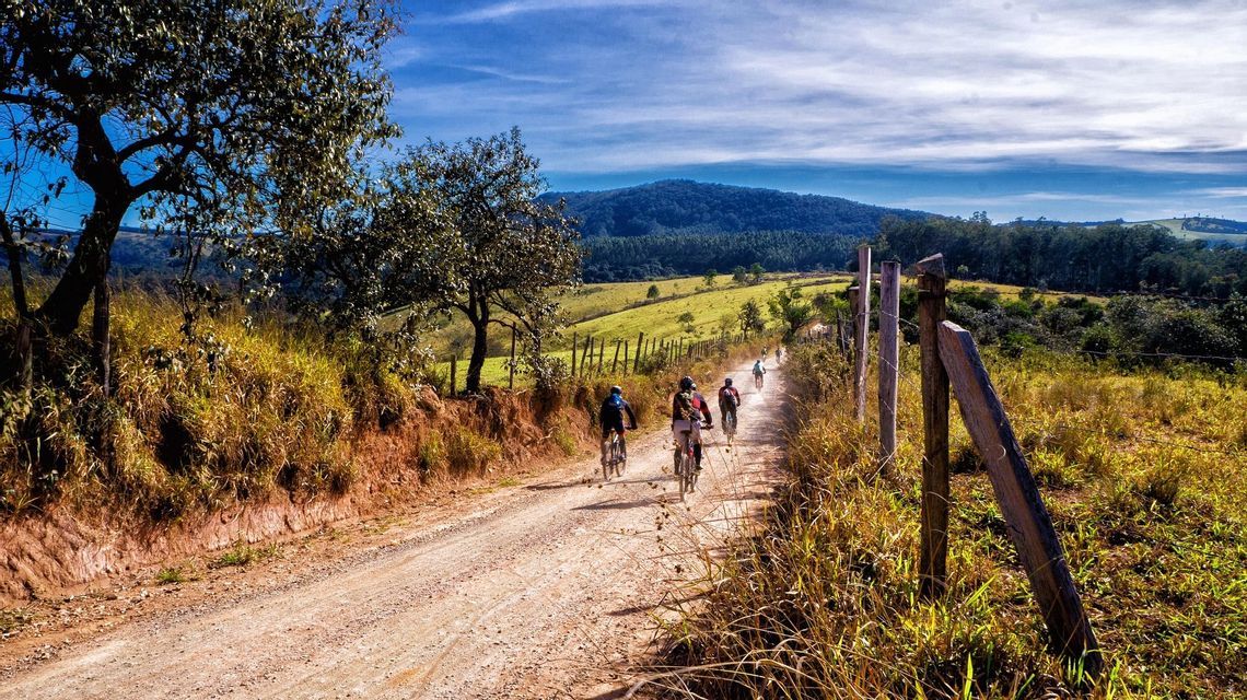 Un gruppo WeRoad percorre in bicicletta un sentiero sterrato in un paesaggio collinare e verdeggiante sotto un cielo azzurro.