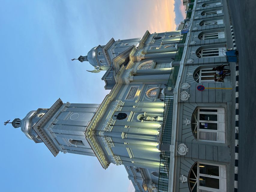 Una gran catedral azul claro con dos torres ornamentadas es iluminada por focos al anochecer.