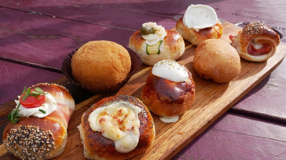 An assortment of savory baked goods and fried appetizers arranged on a wooden board placed on a purple picnic table.