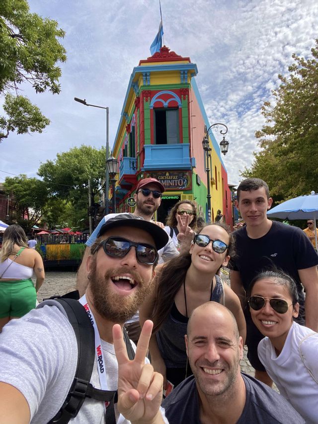Un gruppo WeRoad in viaggio sorride e si fa un selfie su una strada cittadina davanti a un edificio multicolore.