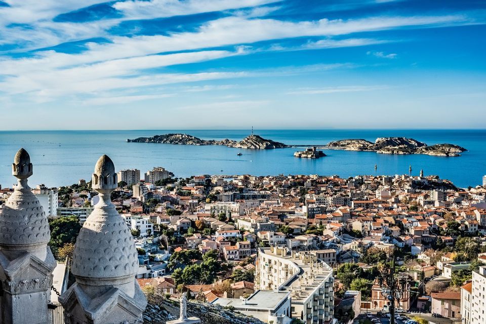 Una vista panorámica desde arriba de una ciudad costera con tejados de tejas rojas, con vistas a un mar azul con varias islas bajo un cielo brillante.