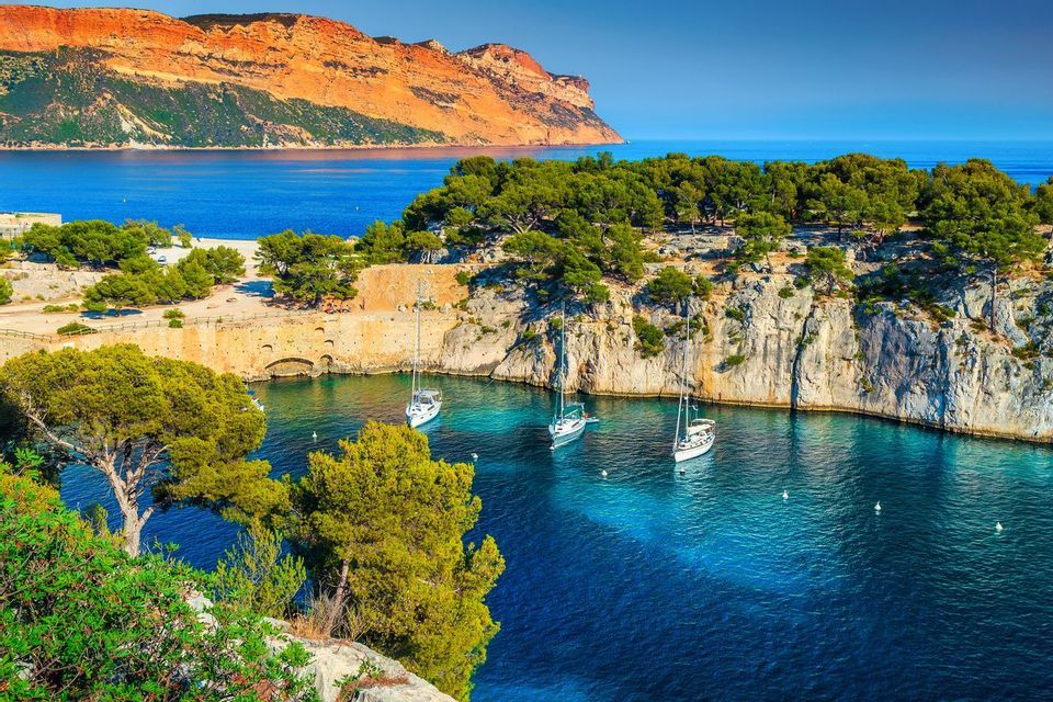 Varios veleros anclados en una cala apartada con agua turquesa, rodeada de acantilados cubiertos de árboles bajo un cielo azul claro.