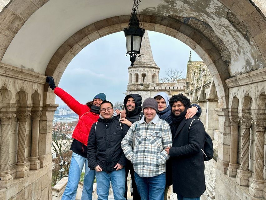 Un voyage de groupe WeRoad de six personnes souriant ensemble sous une arche en pierre, avec un bâtiment historique en arrière-plan.