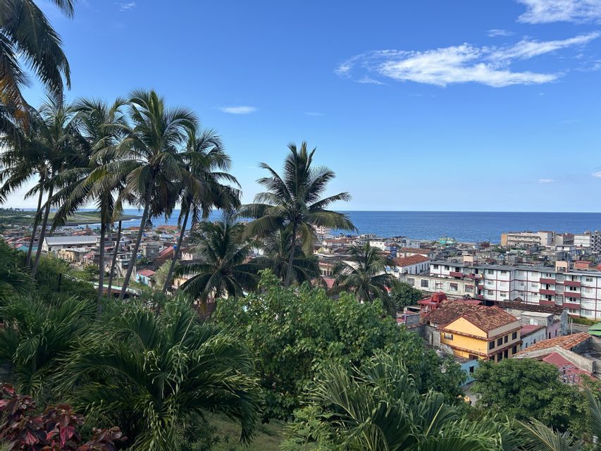 Vista aérea de un pueblo costero con edificios coloridos, enmarcado por palmeras, que se encuentra con el océano azul bajo un cielo despejado.
