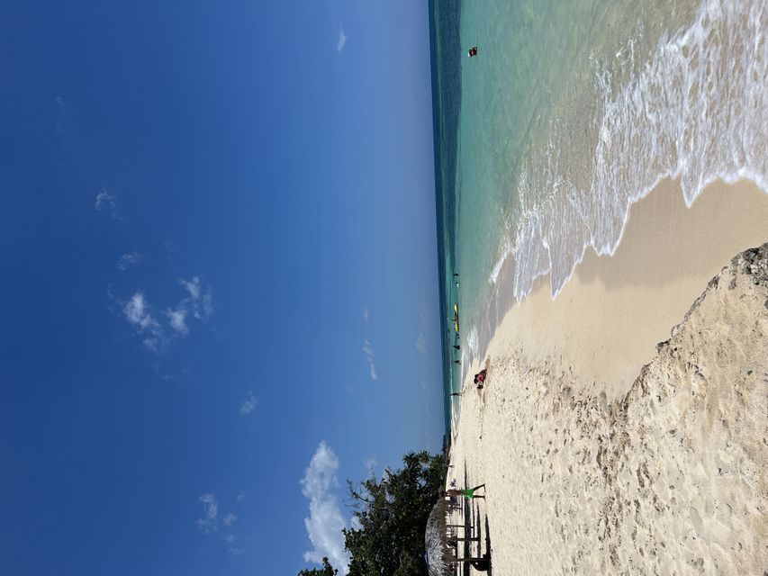 Una vista aérea de una playa de arena blanca con agua turquesa que rompe en la orilla bajo un vasto cielo azul.