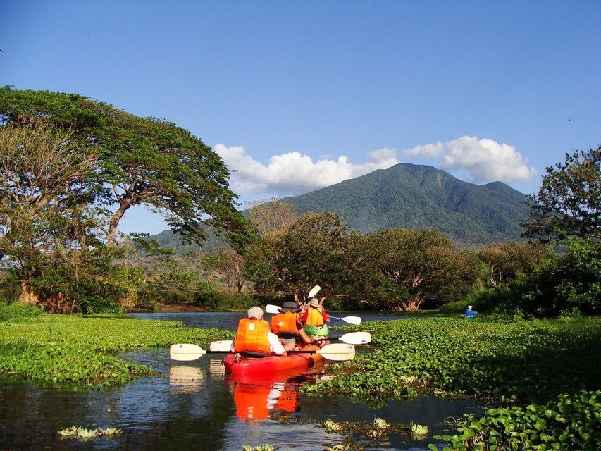 Voyage en groupe WeRoad en kayak sur une rivière paisible couverte de jacinthes d'eau, avec une montagne boisée en arrière-plan.