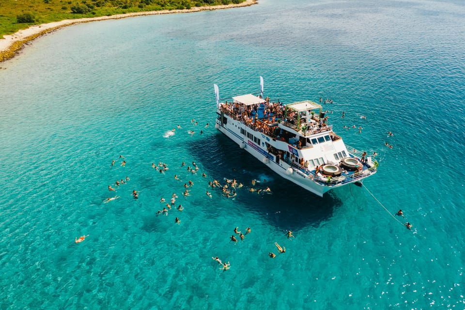 Veduta aerea di un viaggio di gruppo WeRoad su una barca per feste, con persone che nuotano in acqua limpida e turchese.