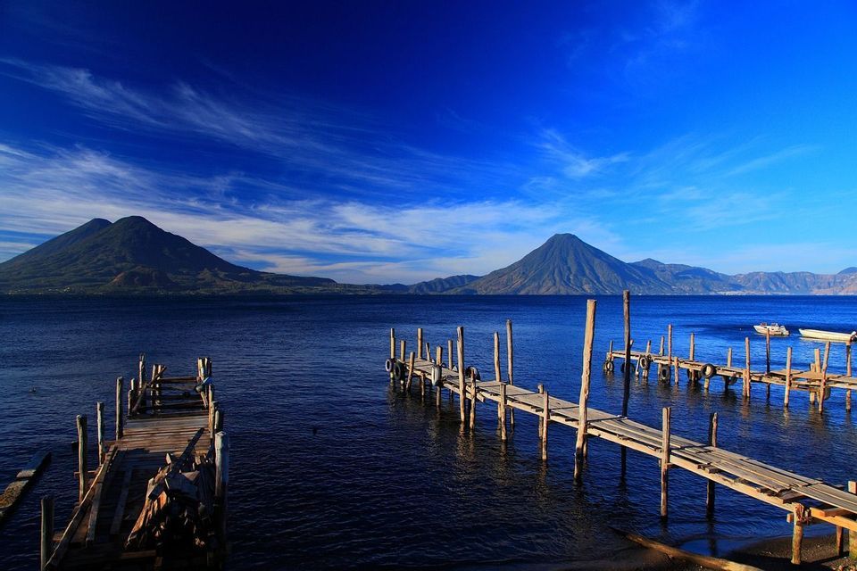 Pontili di legno che si estendono in un lago blu profondo con montagne vulcaniche all'orizzonte sotto un cielo sereno.