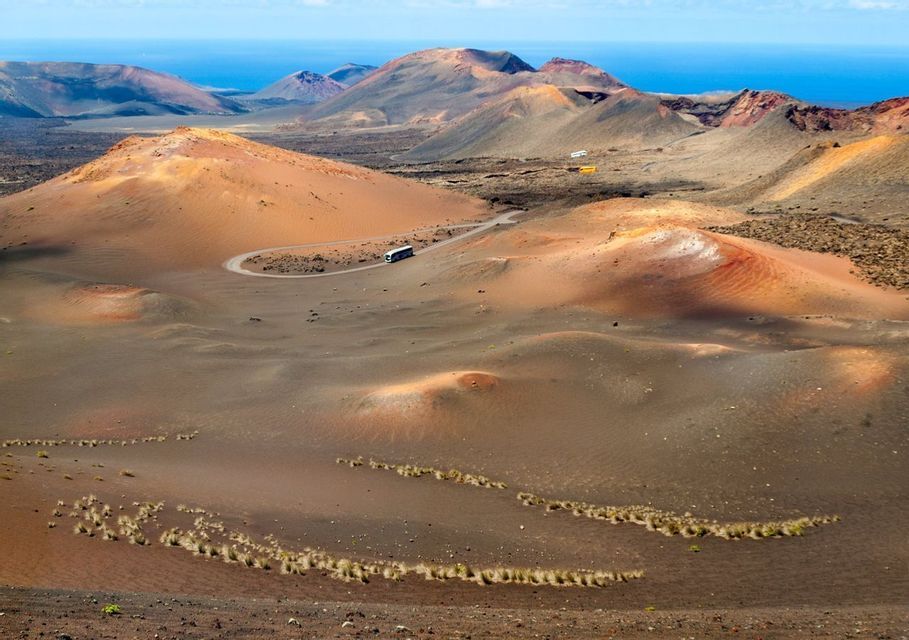 Un pullman turistico percorre una strada tortuosa attraverso un colorato paesaggio vulcanico verso l'oceano.