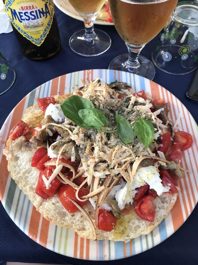 Un piatto di bruschetta condita con pomodori freschi, formaggio e basilico, servita con una bottiglia e bicchieri di birra su un tavolo.