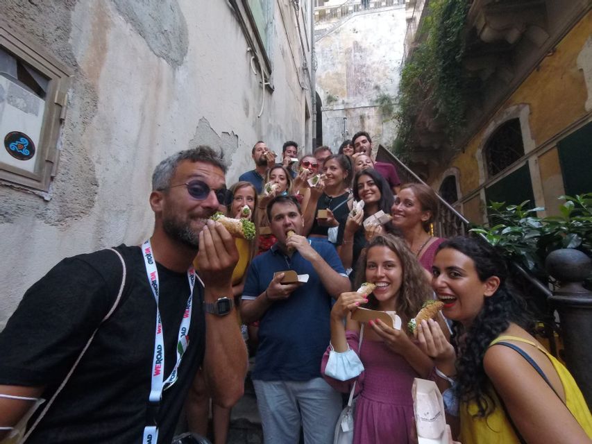 Un viaggio di gruppo WeRoad con persone che sorridono e mangiano cannoli insieme su una stretta scalinata esterna.