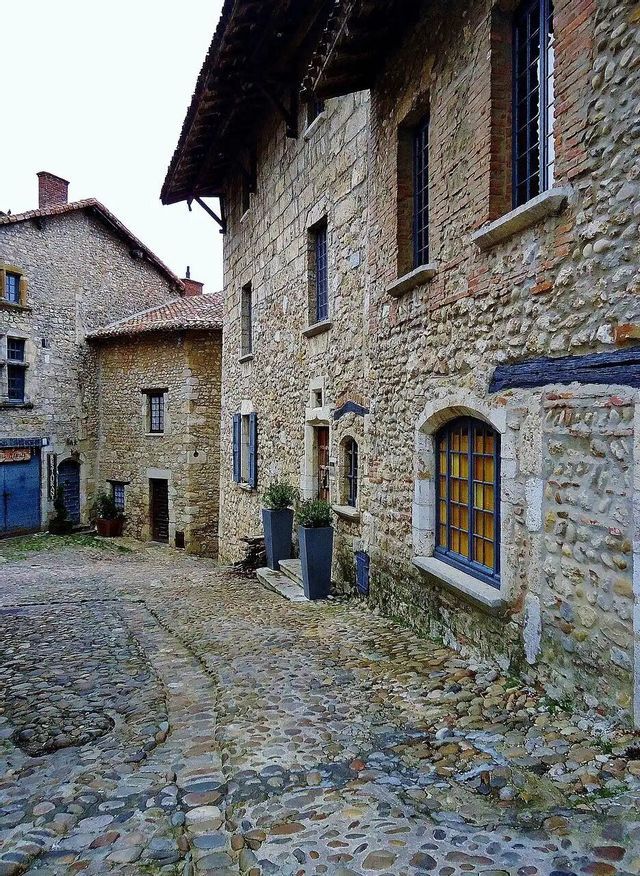Una estrecha calle empedrada serpentea entre edificios históricos de piedra en un antiguo pueblo europeo.