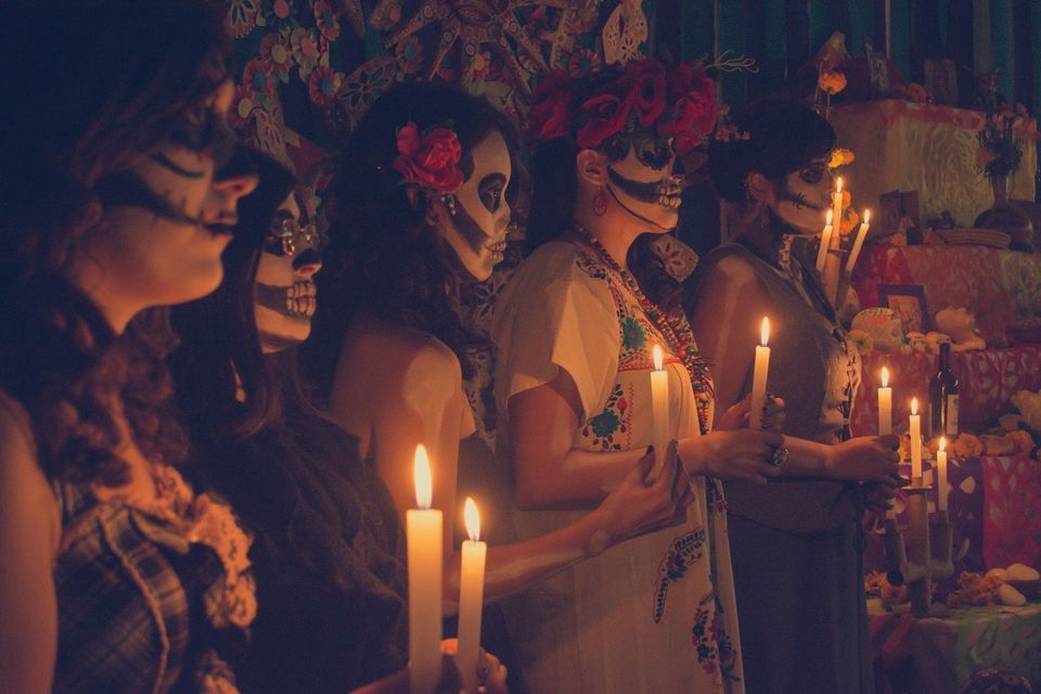 Un viaggio di gruppo WeRoad con volti dipinti da calaveras, che tengono candele accese durante una cerimonia del Giorno dei Morti.