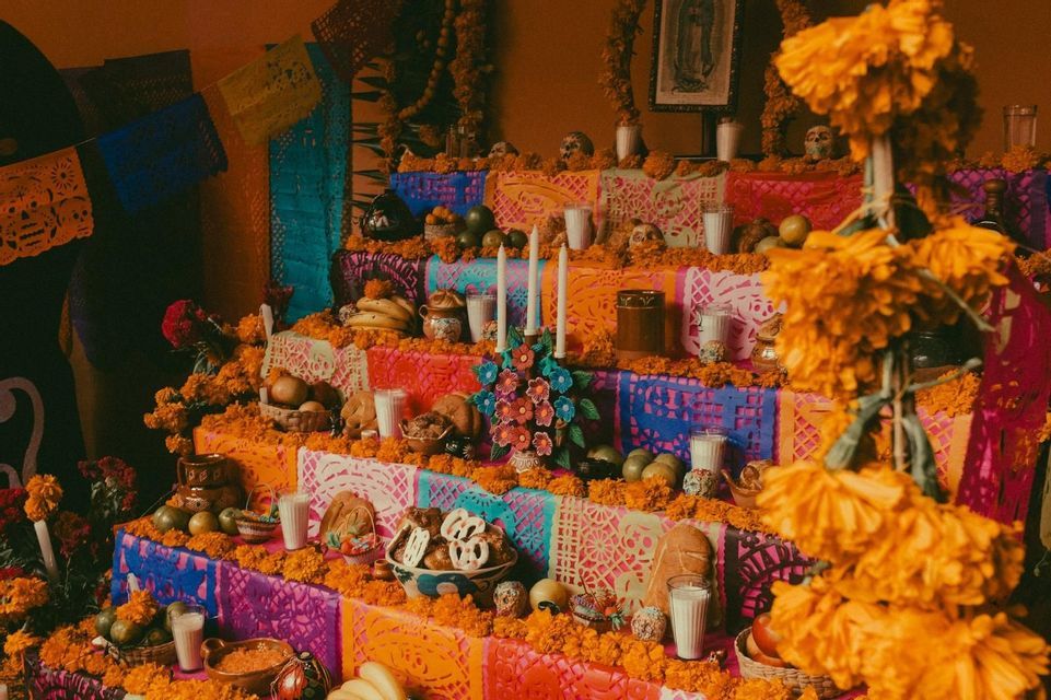 Un'ofrenda del Giorno dei Morti a più livelli decorata con calendule arancioni, teschi di zucchero, candele, cibo e colorato papel picado.