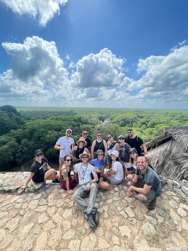Un gruppo WeRoad posa per una foto su un punto panoramico in pietra che si affaccia su una vasta giungla verde sotto un cielo nuvoloso.