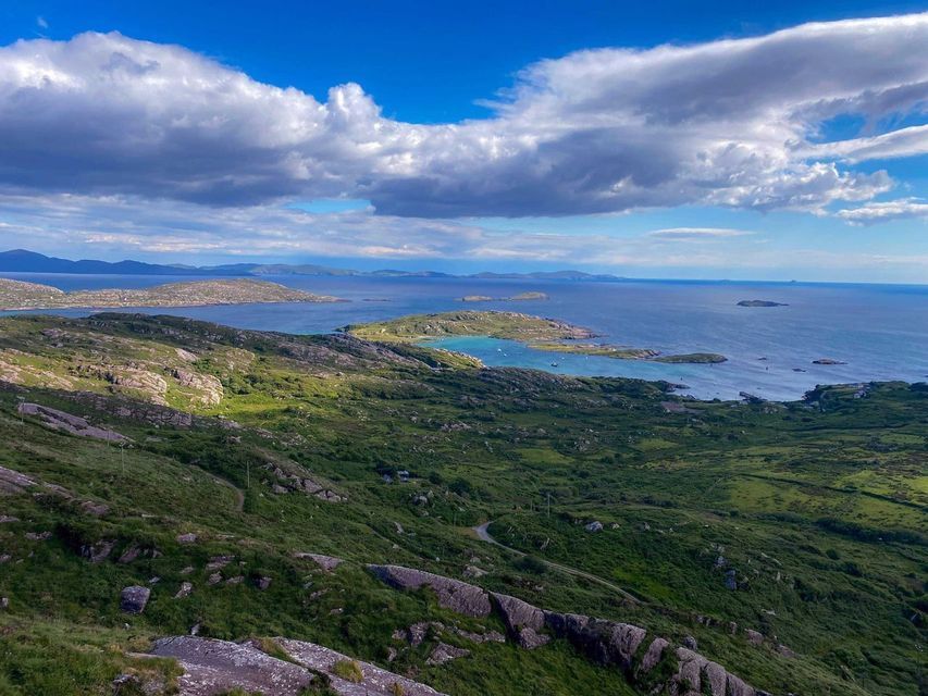 Una vista aérea de una costa rocosa y verde con una bahía turquesa y varias islas pequeñas bajo un cielo parcialmente nublado.