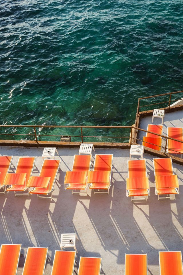 Vista elevada de tumbonas naranjas en una terraza junto al mar turquesa y cristalino.